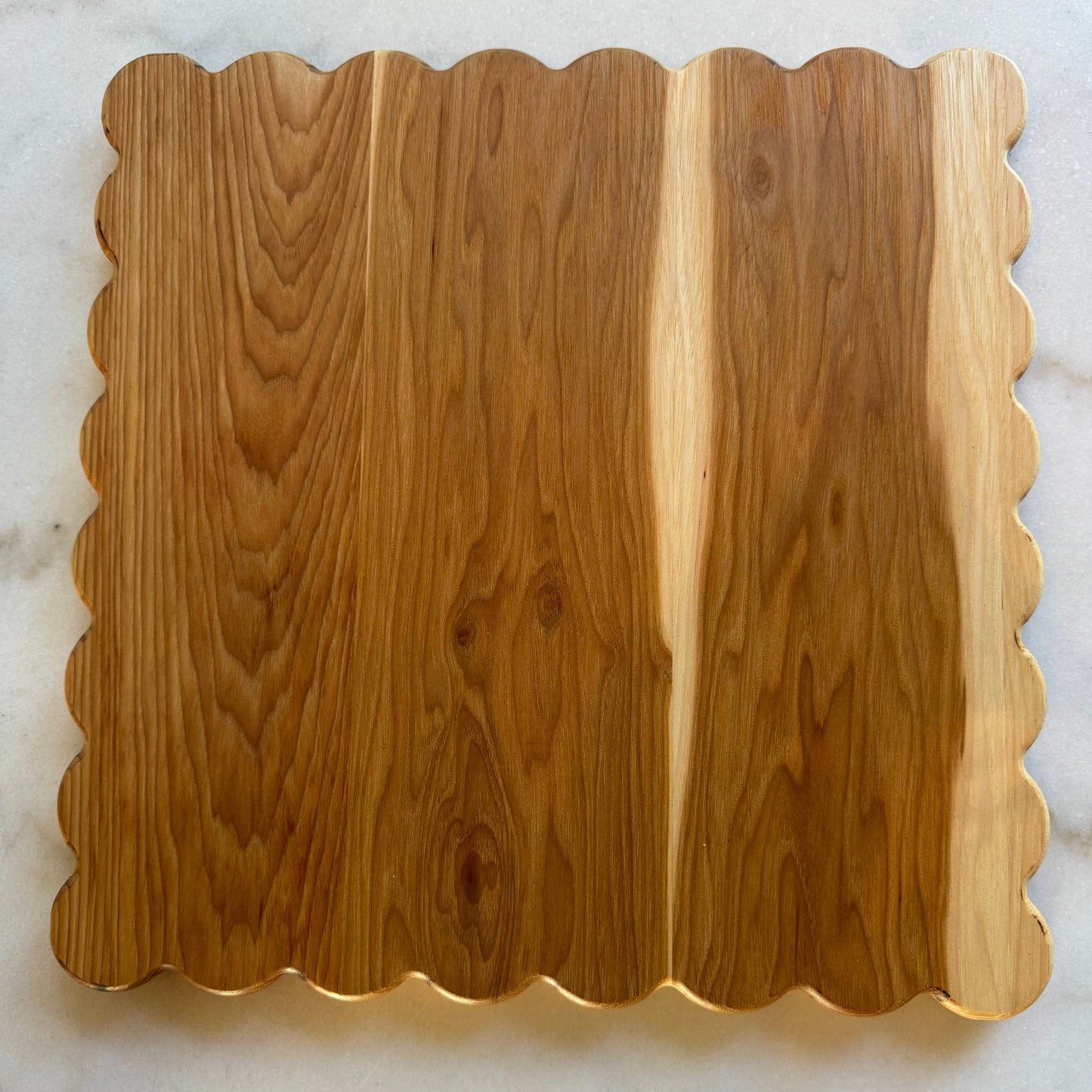 Haylee scalloped-edge hardwood cutting board in hickory, photographed on a marble surface