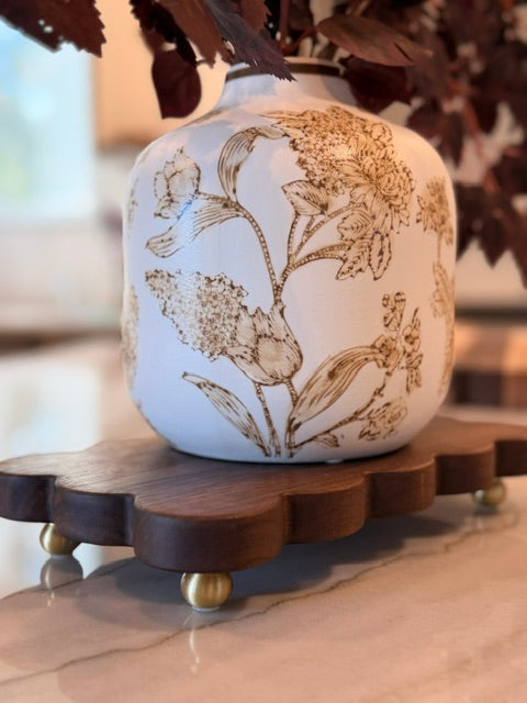 The Dixie dark wood scalloped board on brass feet holding a white and gold floral vase