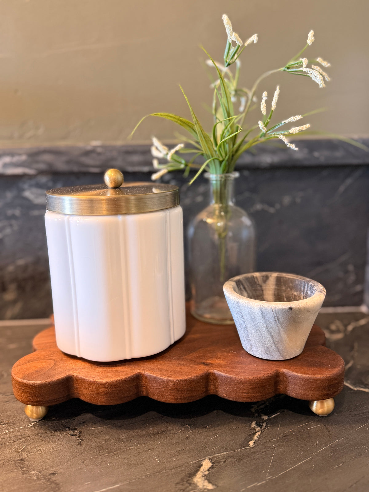 The Dixie scalloped board on brass feet holding a white canister, flowers and a small marble bowl
