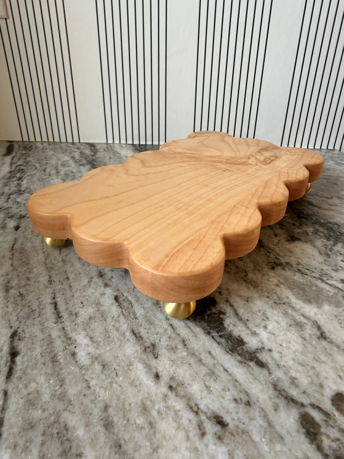 The Dixie scalloped board in light wood on brass feet, side view on a granite counter