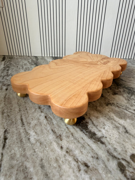The Dixie scalloped board in light wood on brass feet, side view on a granite counter
